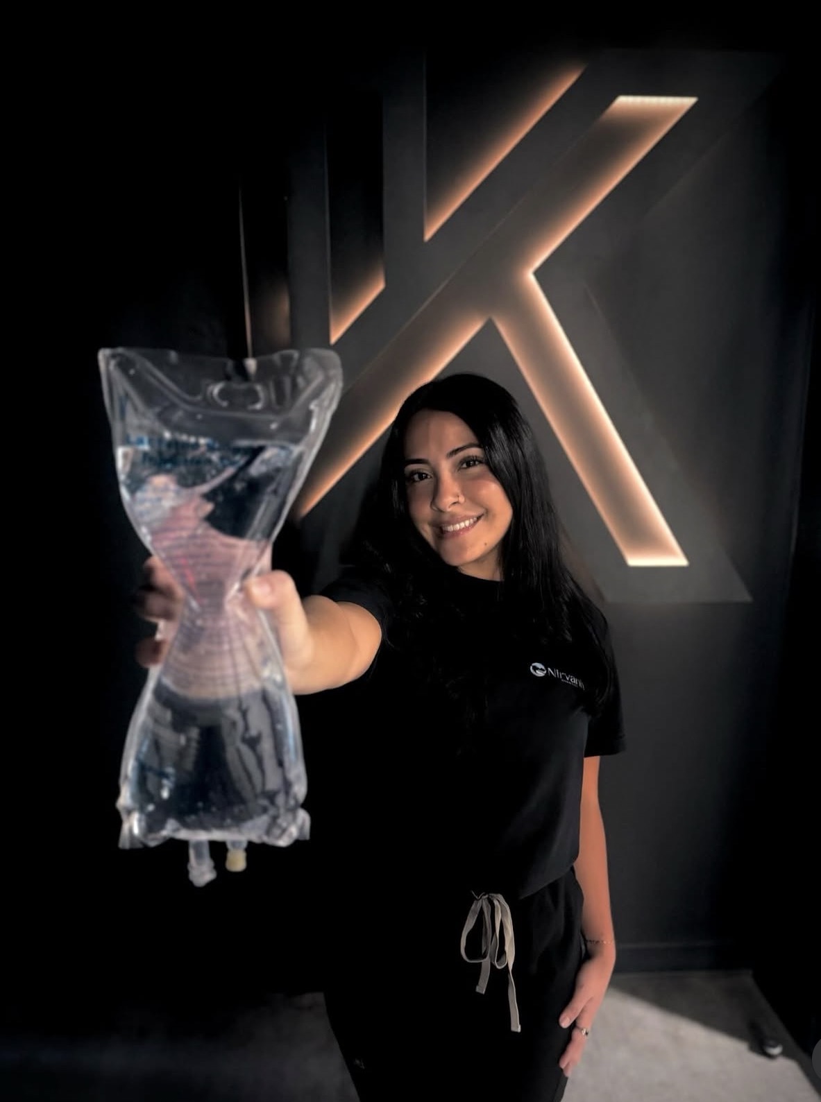 A Kollective clinician holding an IV bag in front of the backlit K wall